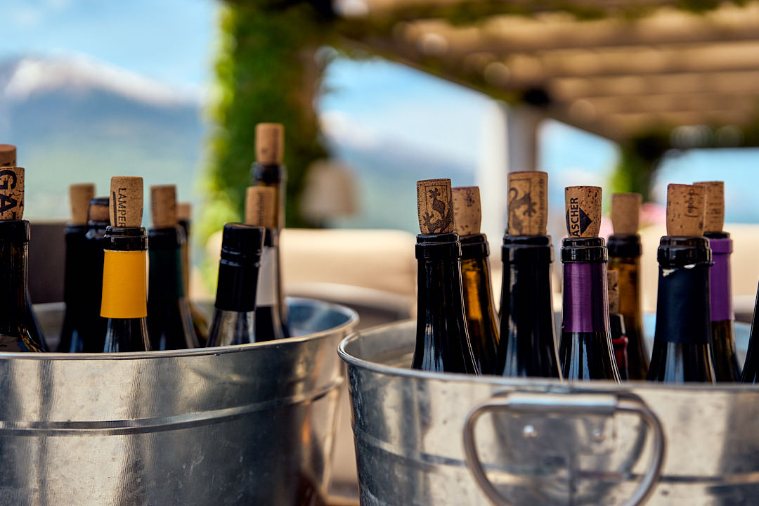Weinflaschen mit Korken in zwei silbernen Eimern auf einem Tisch mit unscharfer Naturkulisse im Hintergrund.