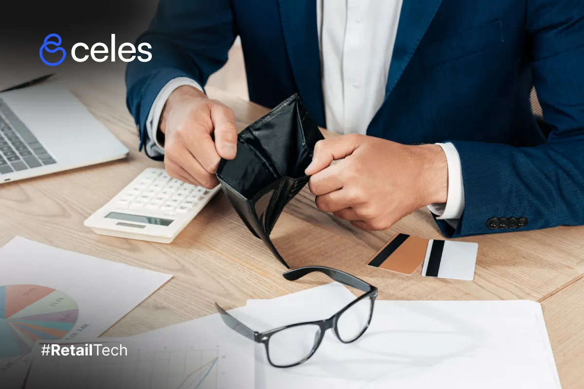 Hombre sosteniendo billetera vacía en oficina: símbolo de presupuestos ajustados en retail tech con laptop y gráficos