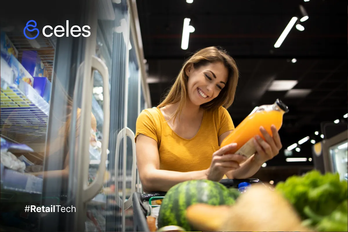 Mujer sonriente con cabello rubio largo, vistiendo camiseta amarilla, selecciona jugo de naranja fresco en estante de supermercado refrigerado con iluminación LED, carrito con sandía y verduras frescas, ambiente moderno de Retail Tech.