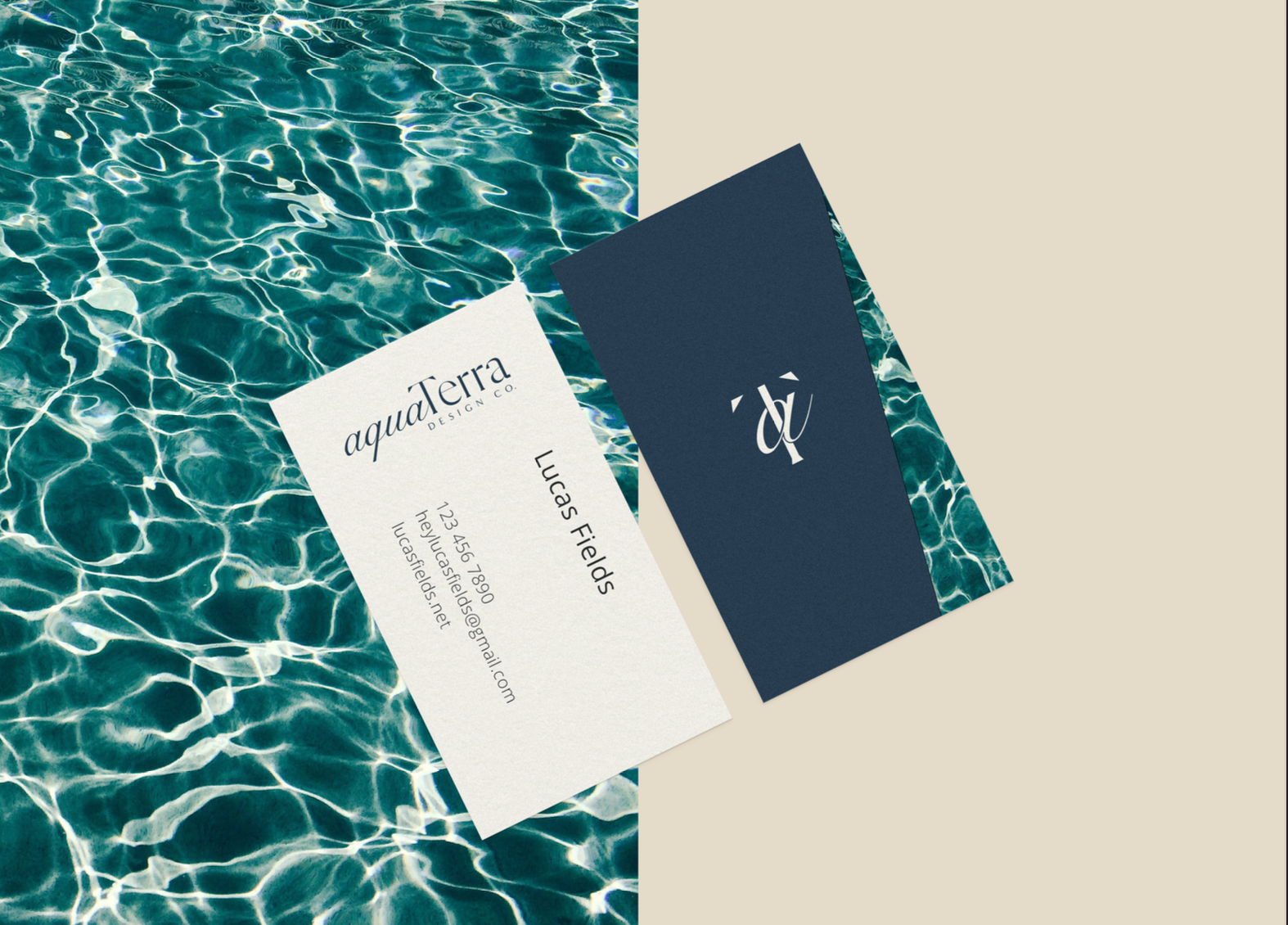 AquaTerra Design Co. business cards in cream and navy, laid over pool water and sand