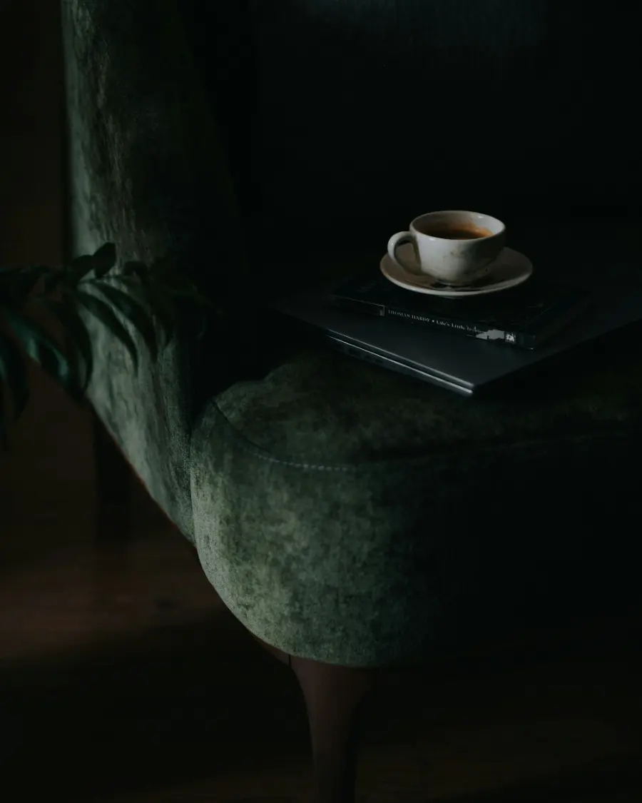 A cup of coffee beside a green velvet chair