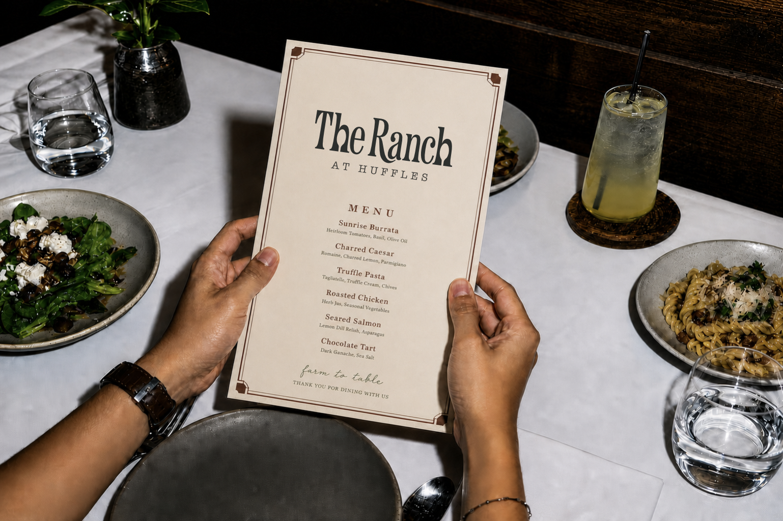 Diner holding a printed The Ranch at Huffles menu at a table set with salad, pasta and drinks