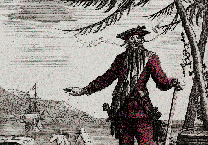 Antique engraving of Blackbeard on a beach, smoke rising from fuses under his hat, his ship anchored behind him