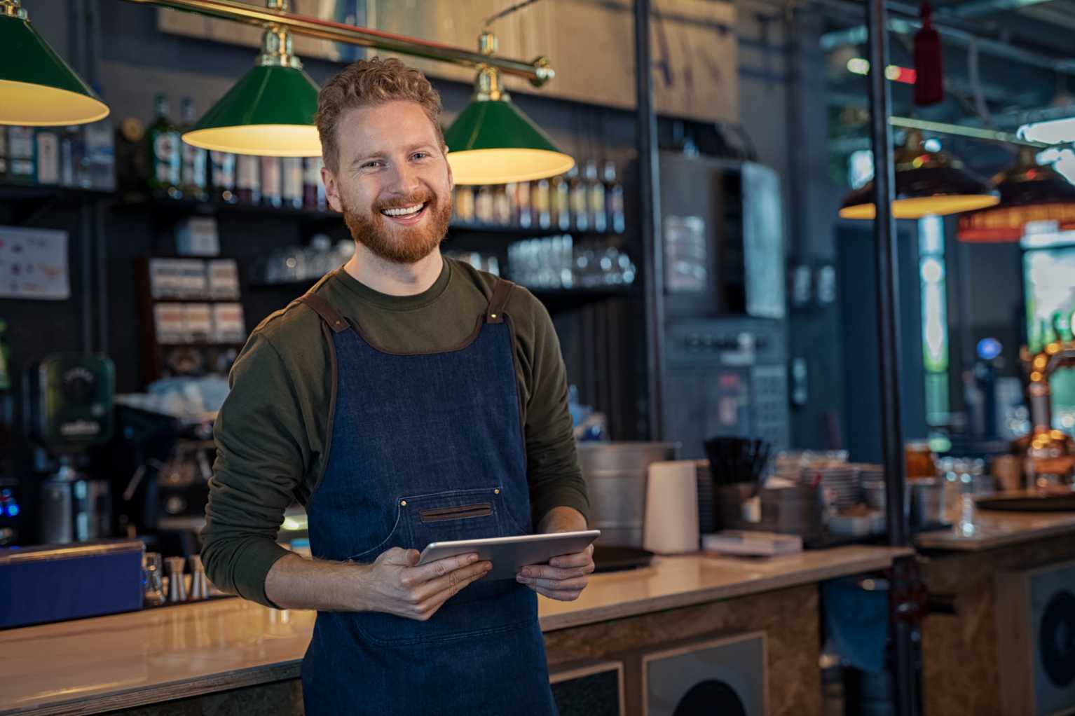 smiling waiter in green top holding a smartphone