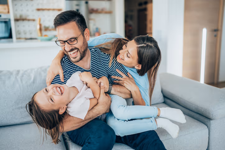 A dad and mother reaching around their daughter, all smiling as they appear to be having fun