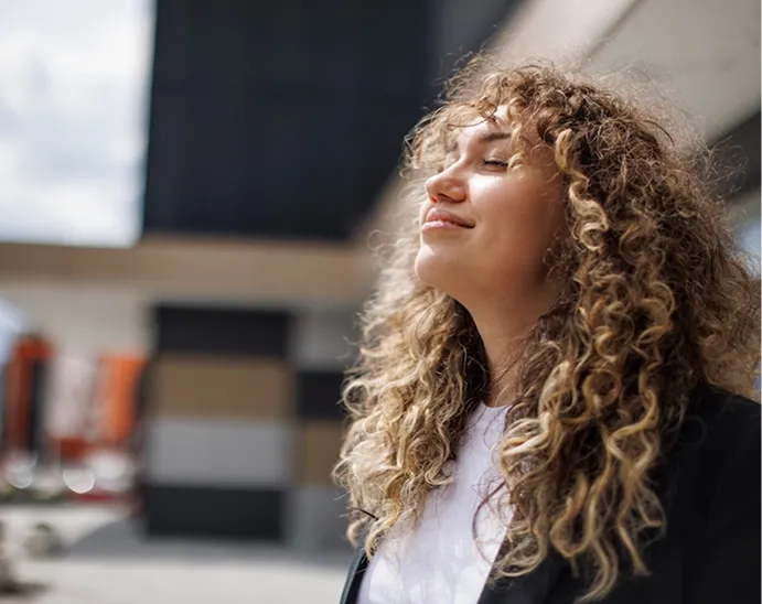 Person standing outdoors in natural light, appearing calm and relaxed near a modern building