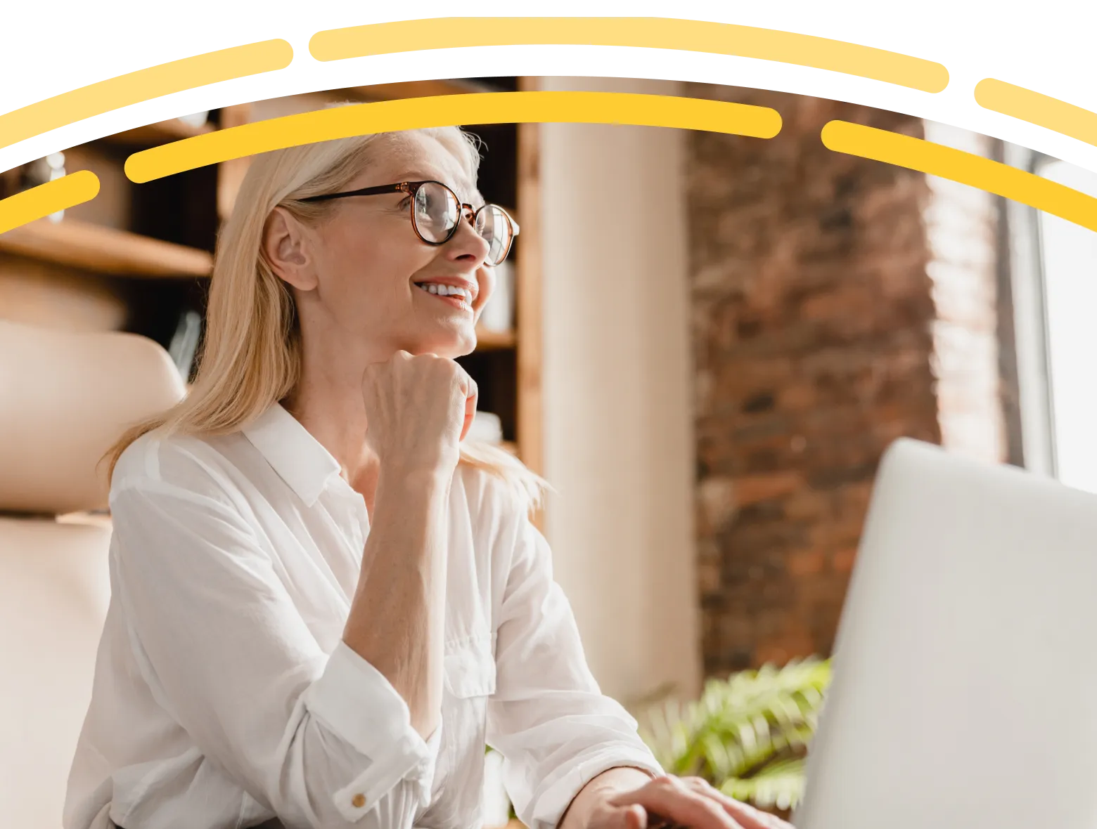 Smiling older woman wearing glasses, seated at a desk in a bright home office