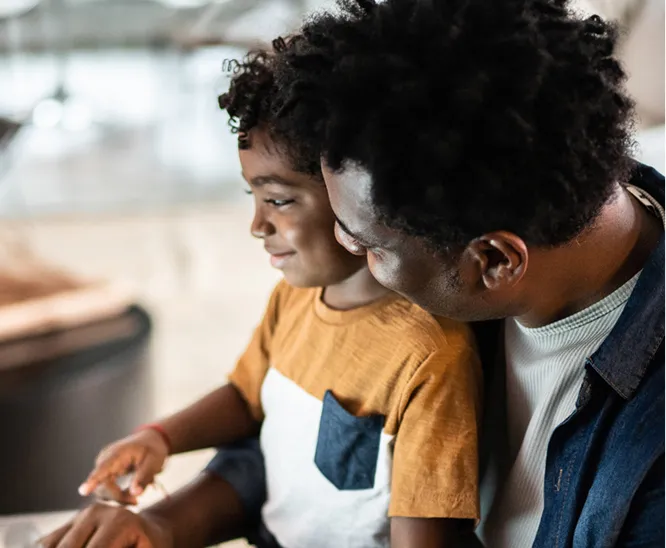 Adult sitting with a young child, guiding them while using a tablet together