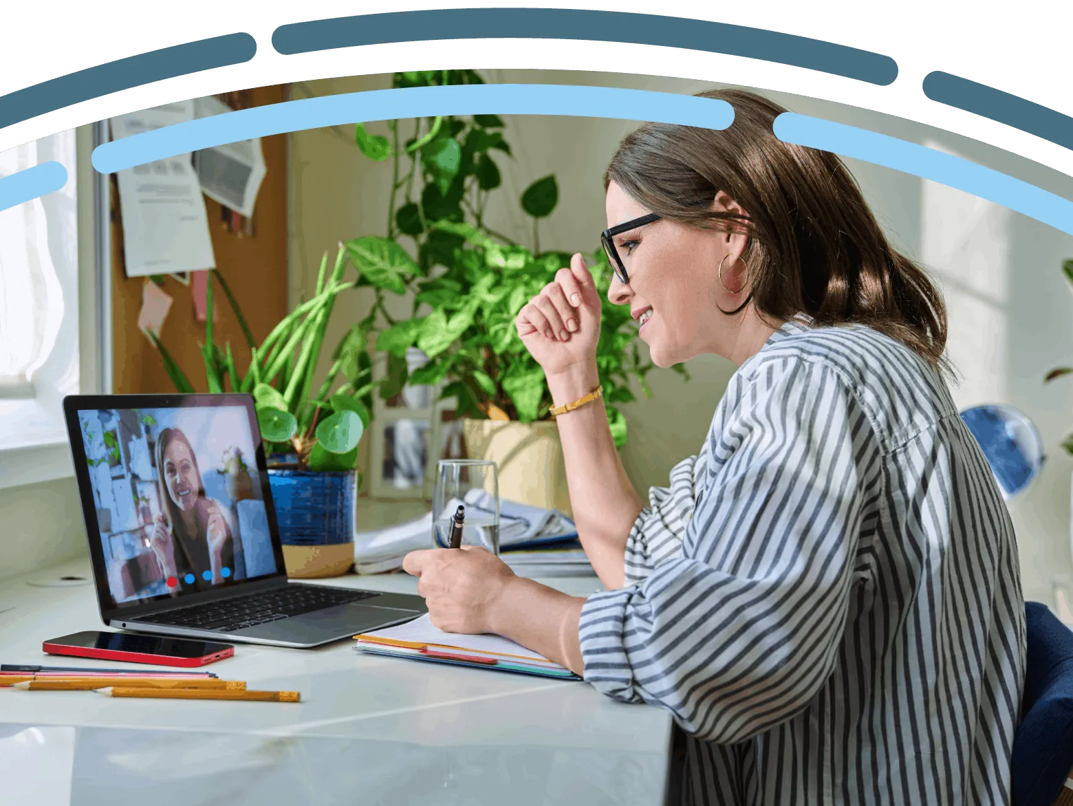 A woman participates in a virtual healthcare appointment from her home, taking notes during a video call.