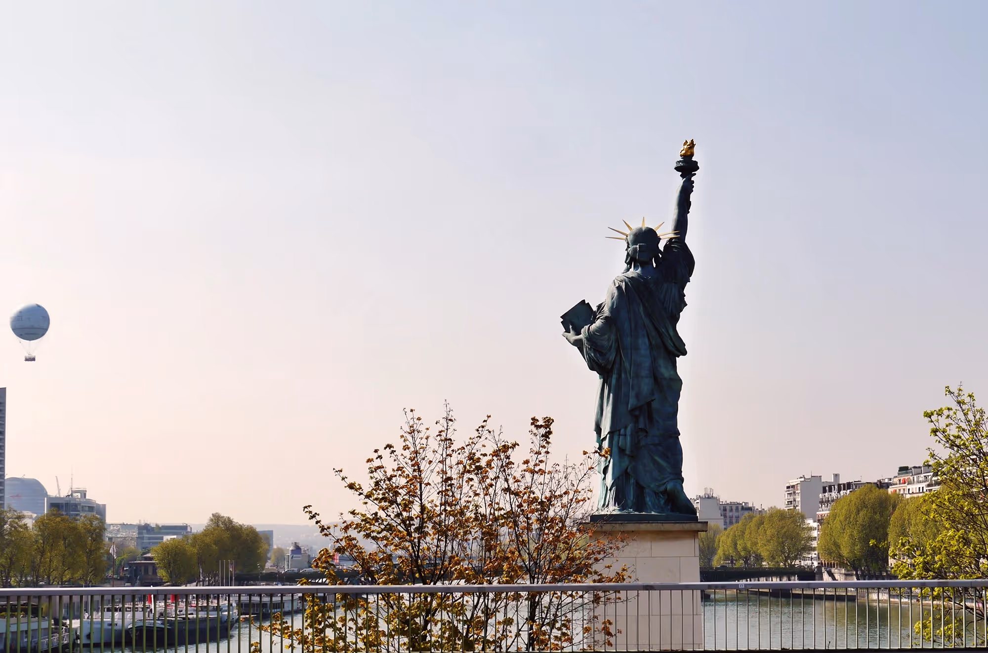 statue of liberty from the back in front of water with a small hot air baloon on the left