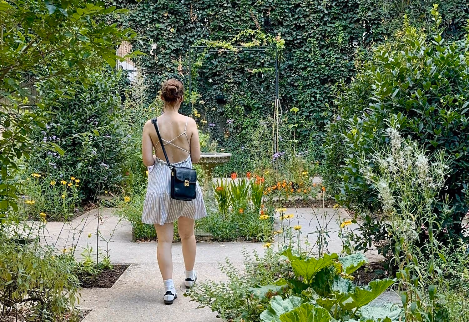 Ladyin a dress turning her back to the camera looking at a garden
