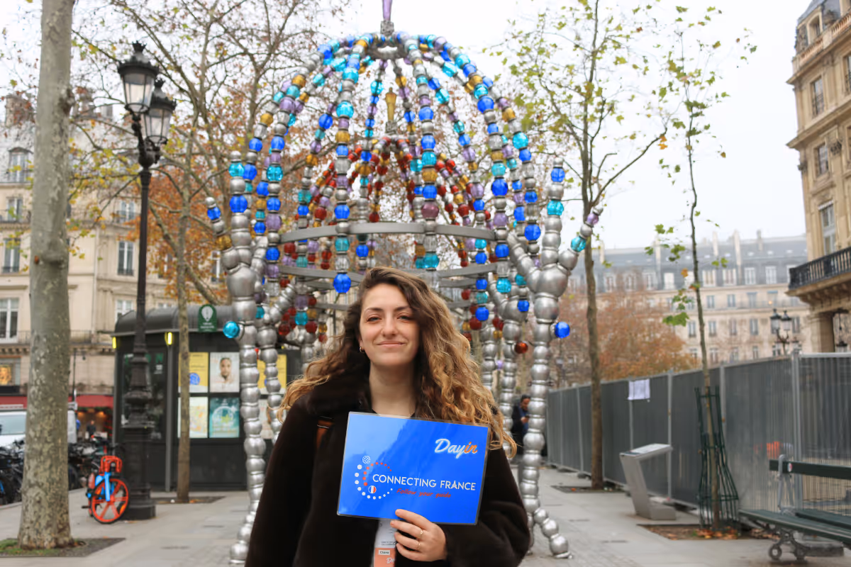 Guide holding a blue sign saying "Dayin" and "Connecting France" in front of a big and colorful glass-bubble modern sculpture.