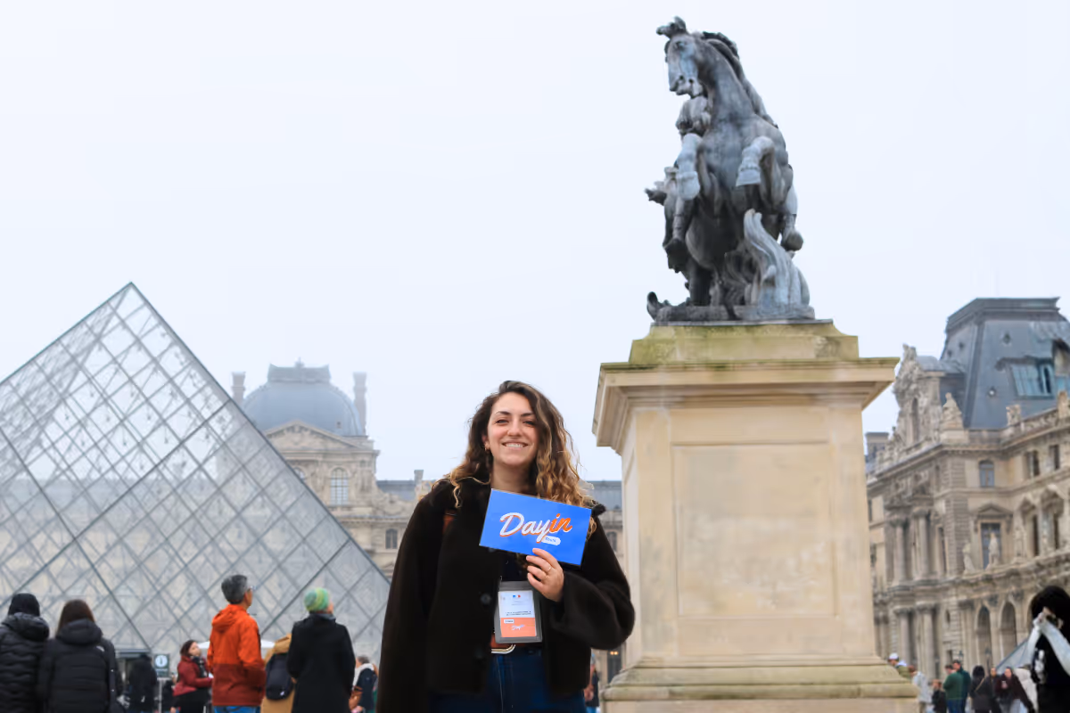 Guide holding a blue sign saying "Dayin" and "Connecting France" in front of a big and colorful glass-bubble modern sculpture.