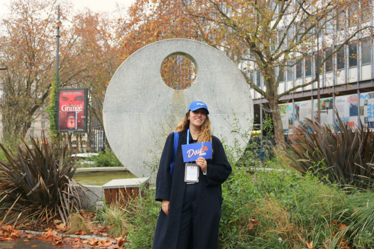 Guide holding a blue sign saying "Dayin" and "Connecting France" in front of a big and colorful glass-bubble modern sculpture.