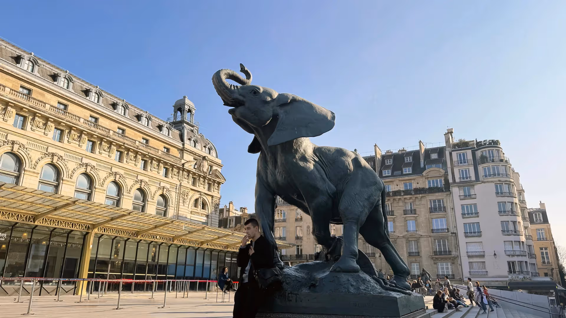 Guide holding a blue sign saying "Dayin" and "Connecting France" in front of a big and colorful glass-bubble modern sculpture.