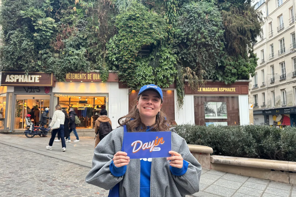 Guide holding a blue sign saying "Dayin" and "Connecting France" in front of a big and colorful glass-bubble modern sculpture.