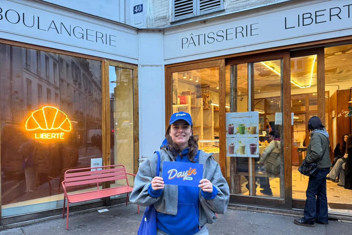 Guide holding a blue sign saying "Dayin" and "Connecting France" in front of a big and colorful glass-bubble modern sculpture.