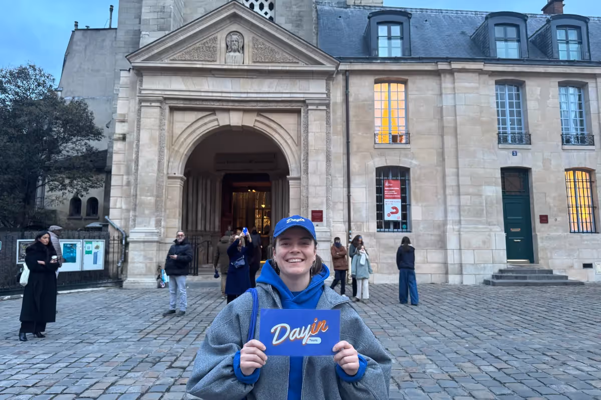 Guide holding a blue sign saying "Dayin" and "Connecting France" in front of a big and colorful glass-bubble modern sculpture.