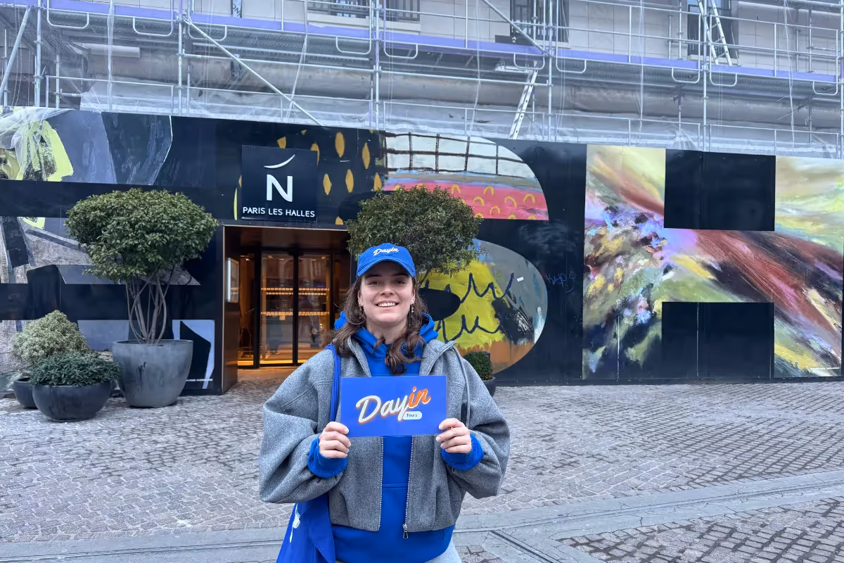 Guide holding a blue sign saying "Dayin" and "Connecting France" in front of a big and colorful glass-bubble modern sculpture.