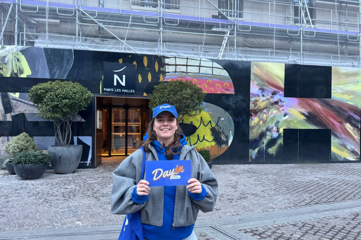 Guide holding a blue sign saying "Dayin" and "Connecting France" in front of a big and colorful glass-bubble modern sculpture.