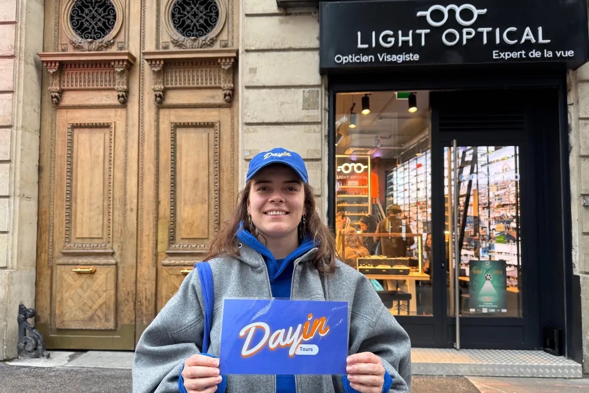 Guide holding a blue sign saying "Dayin" and "Connecting France" in front of a big and colorful glass-bubble modern sculpture.