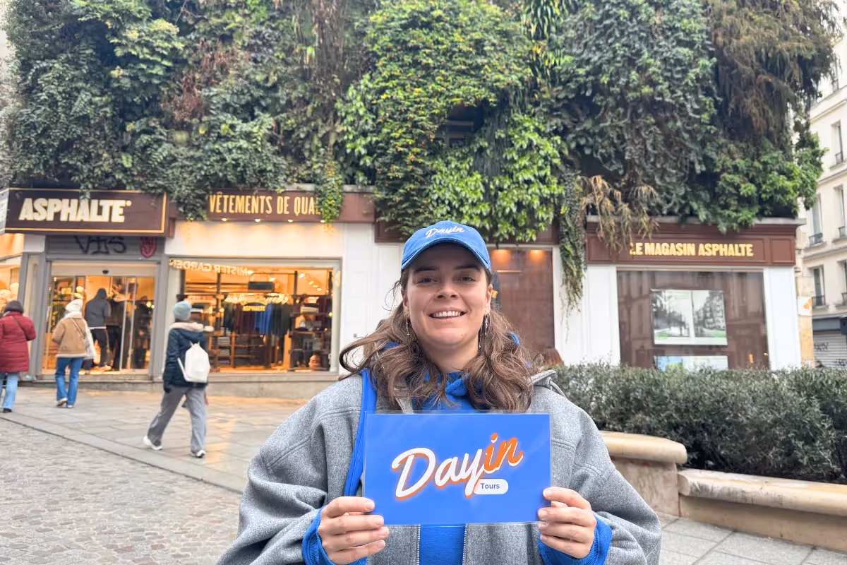 Guide holding a blue sign saying "Dayin" and "Connecting France" in front of a big and colorful glass-bubble modern sculpture.