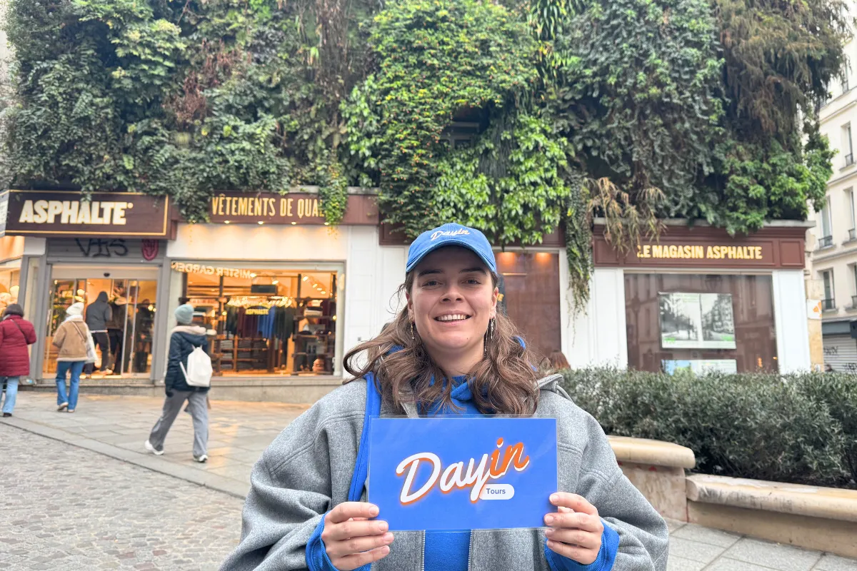 Guide holding a blue sign saying "Dayin" and "Connecting France" in front of a big and colorful glass-bubble modern sculpture.