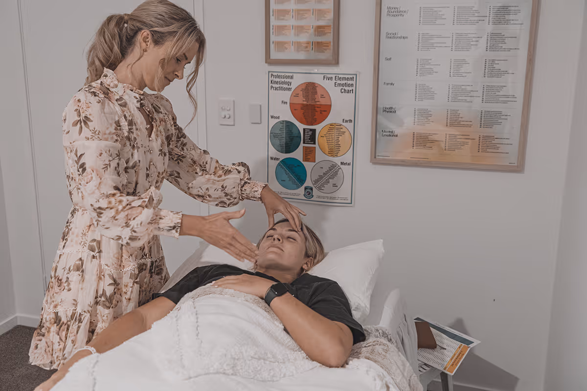 A woman in a floral dress performing a kinesiology session on a client lying on a treatment table.