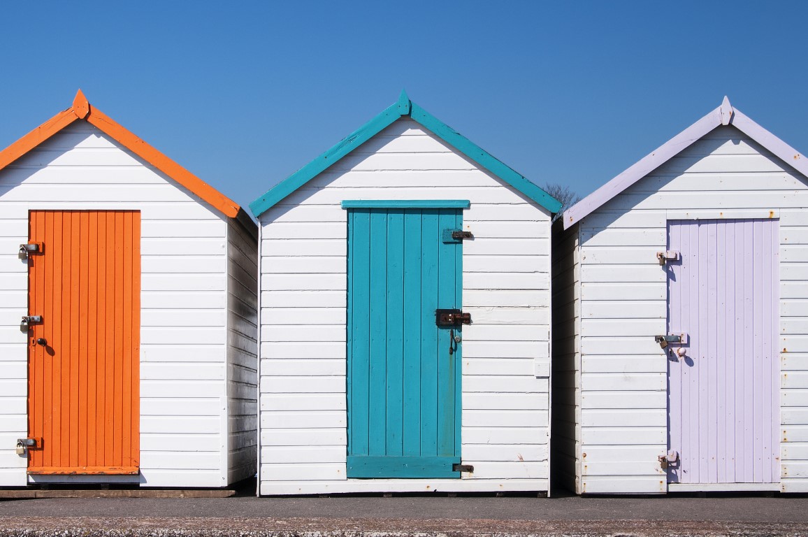 A set of three colorful beach huts at Paignton, Devon, UK on a sunny day.