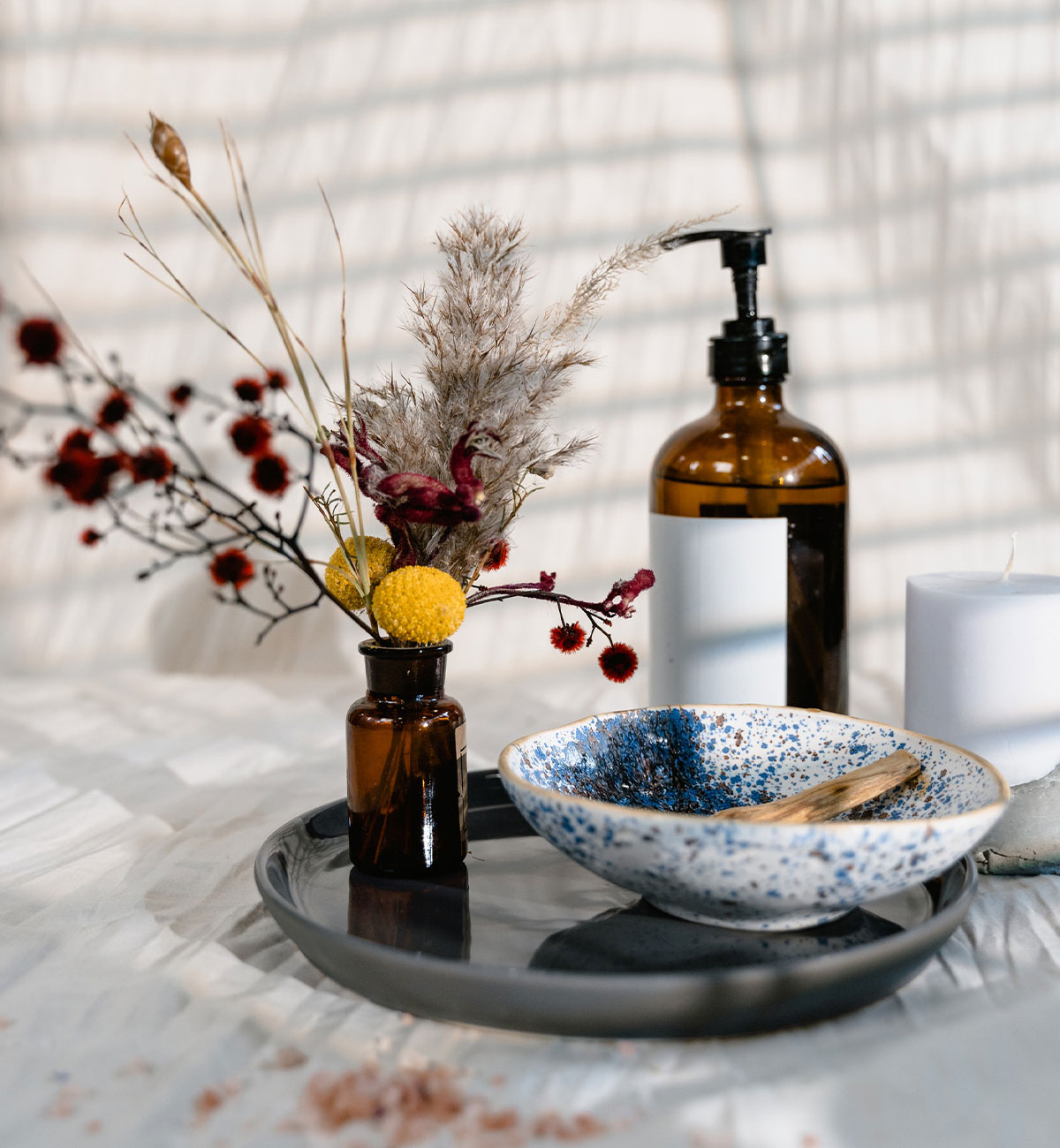 A tray on a table with cosmetic products and vase with flowers.