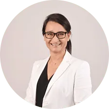 Smiling woman with dark hair tied back, wearing glasses, a white blazer, and a black top.