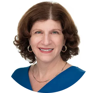 Smiling middle-aged woman with curly brown hair wearing hoop earrings and a blue top against a white background.
