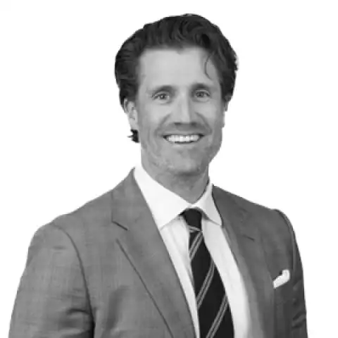 Smiling man with wavy hair in a suit and striped tie against a white background.