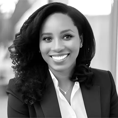 Black and white portrait of a woman with curly hair, wearing a blazer and smiling at the camera.