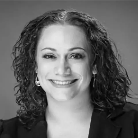 Black and white portrait of a smiling woman with curly hair wearing earrings and a dark blazer.