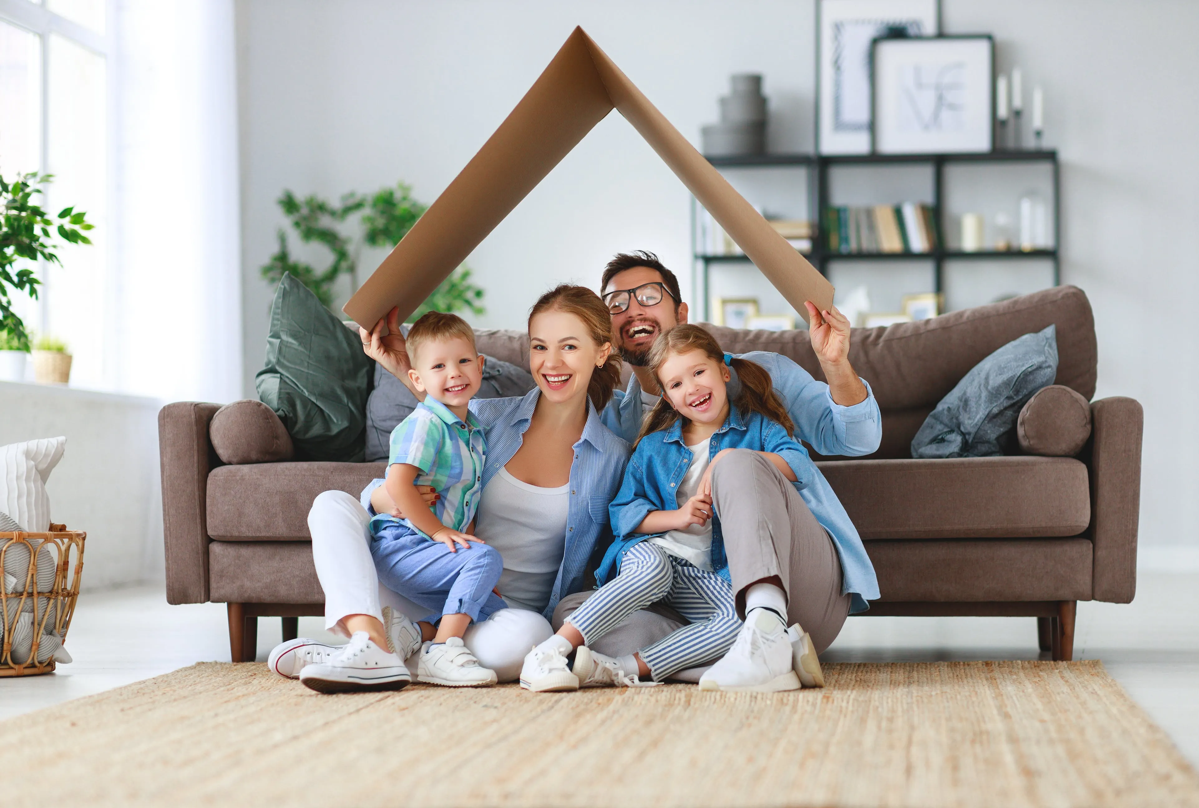 Family in their living room sitting in front of the couch holding a cartboard as a roof above their heads