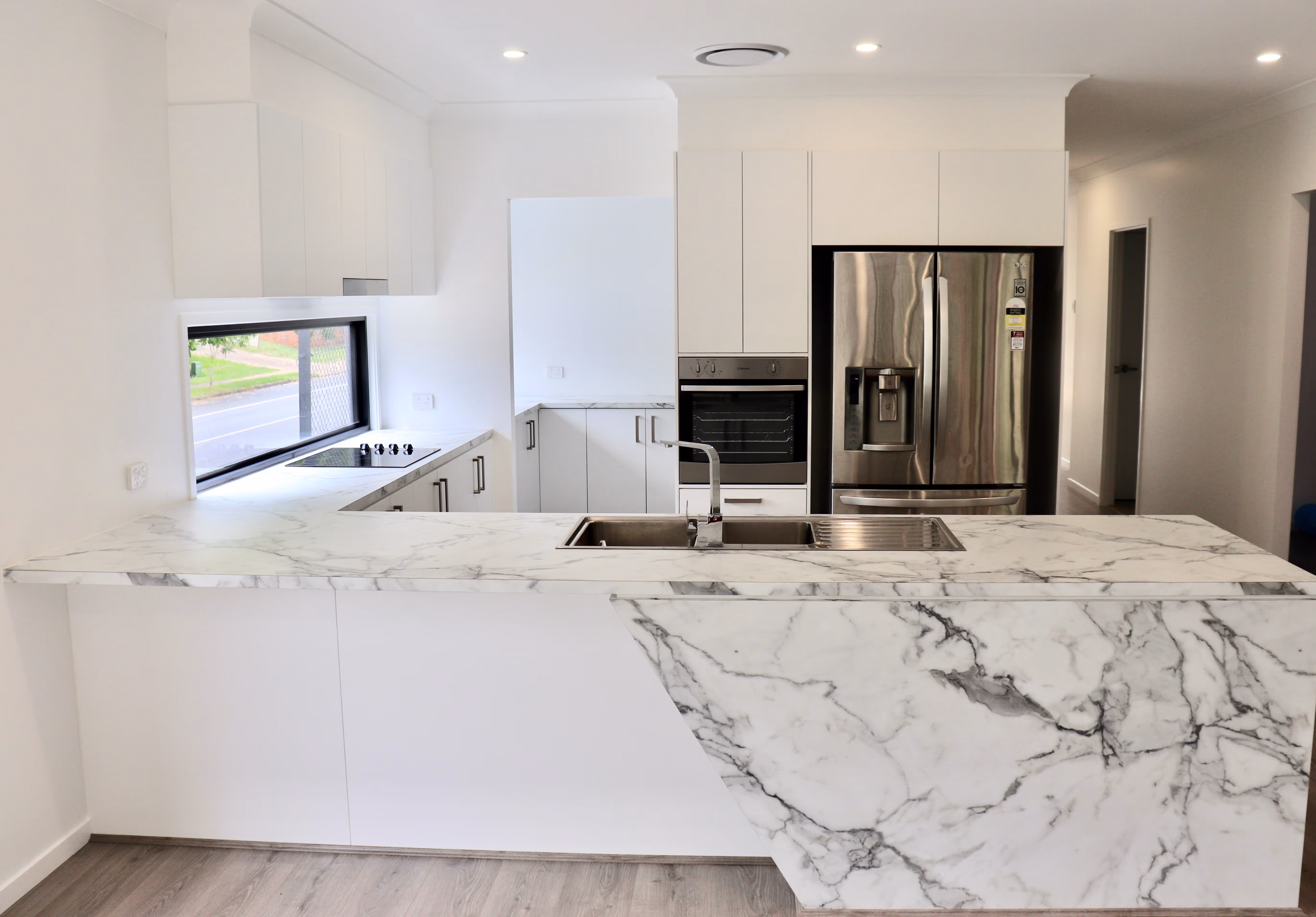 Modern kitchen with white marble countertops, stainless steel sink, built-in oven, stovetop, and refrigerator.