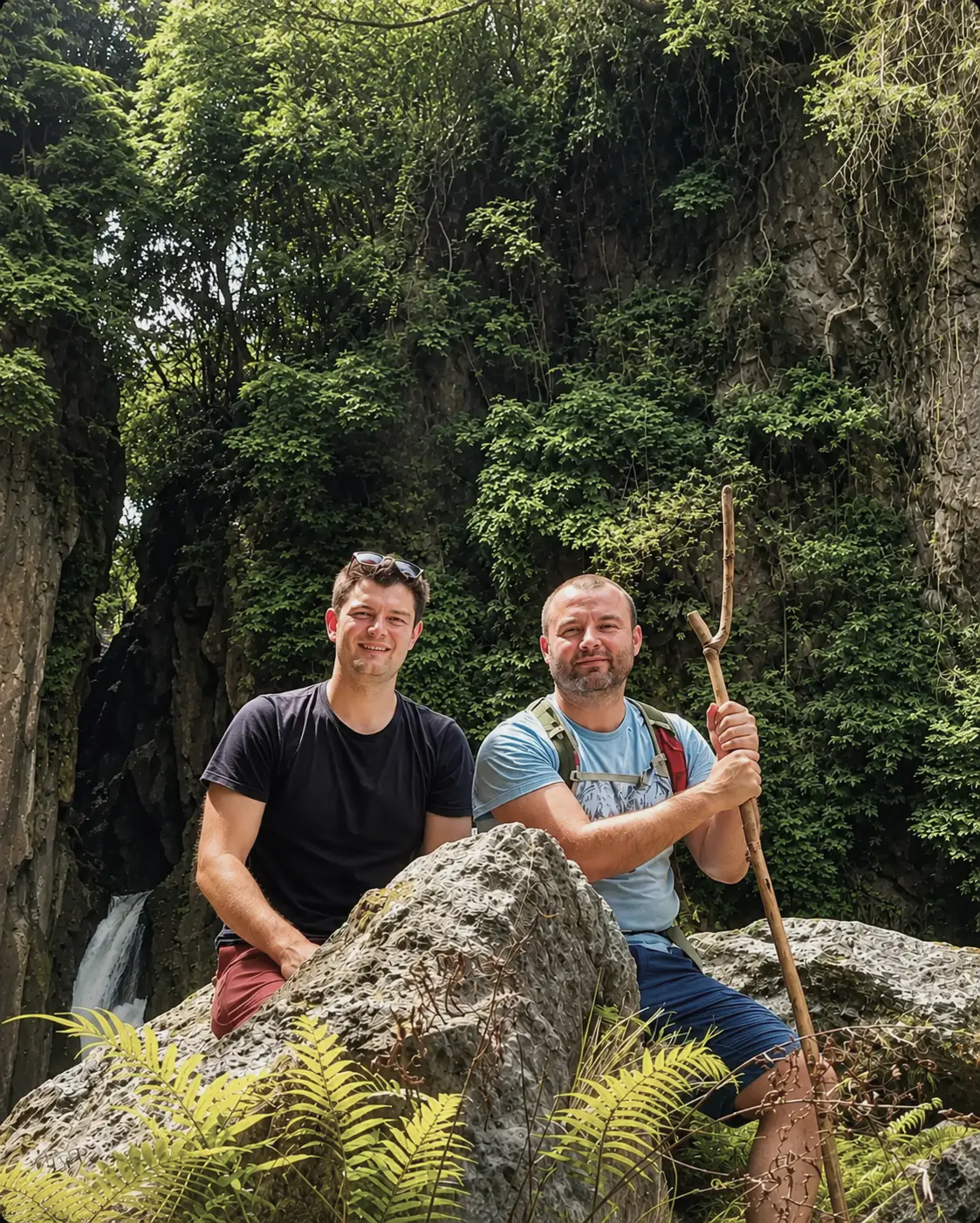 Rob Lynch and Rob Woodhead, founders of Old.St Labs, sit on large rocks in a lush rainforest gorge beside a small waterfall. One man holds a walking stick while both smile toward the camera. Dense greenery, ferns, and steep rock walls surround them, creating a rugged outdoor adventure setting.