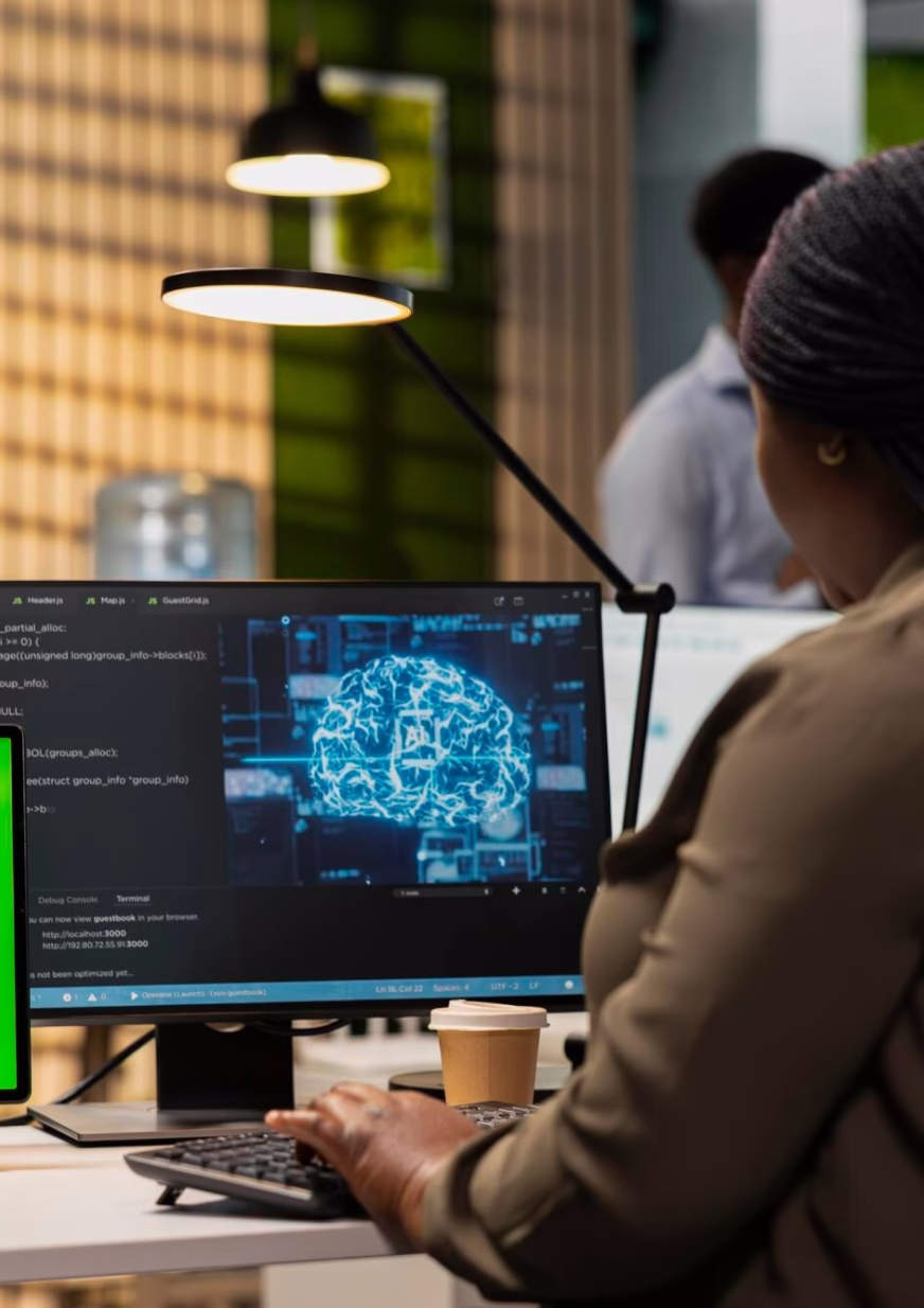 Person working on a computer displaying a digital brain graphic and programming code in an office.