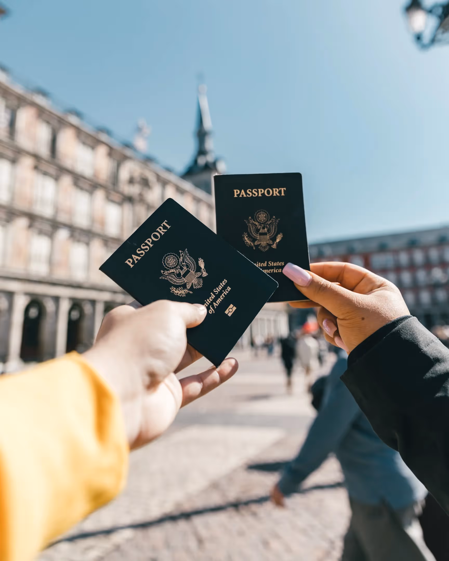 Image shows to hands holding passports in front of a monument