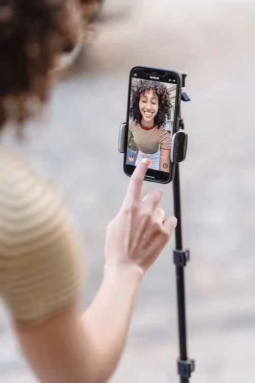 FreeShort-Form Video Content For Influencer Marketing Campaigns Crop positive ethnic female touching screen of smartphone while recording live video on street with paved sidewalk on blurred background Stock Photo
