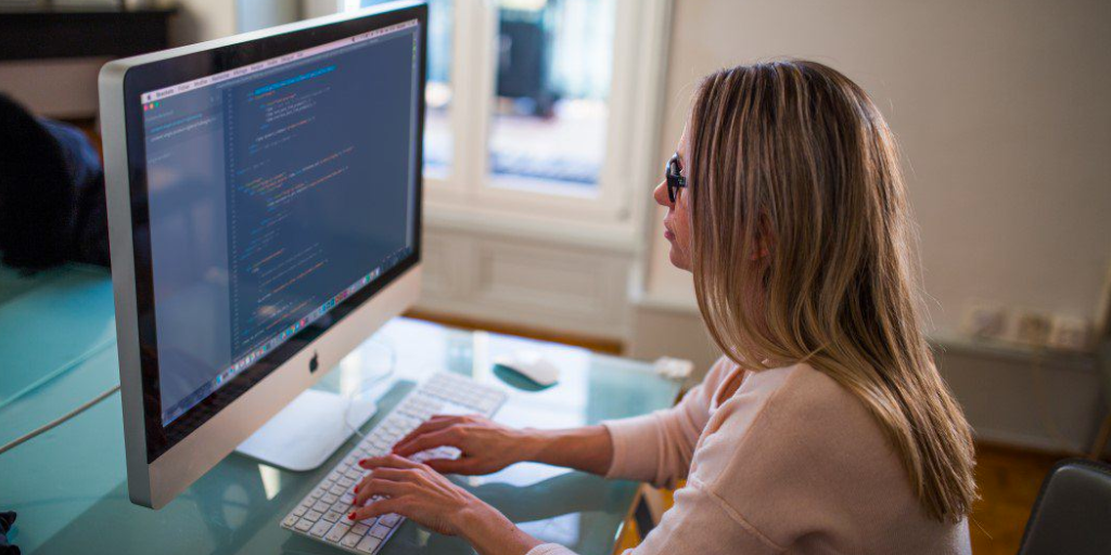 Photo of a woman sitting in front of a computer writing code