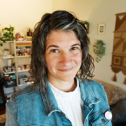 Malia Hagen, a therapist, stands smiling in her office with books and plants all around.