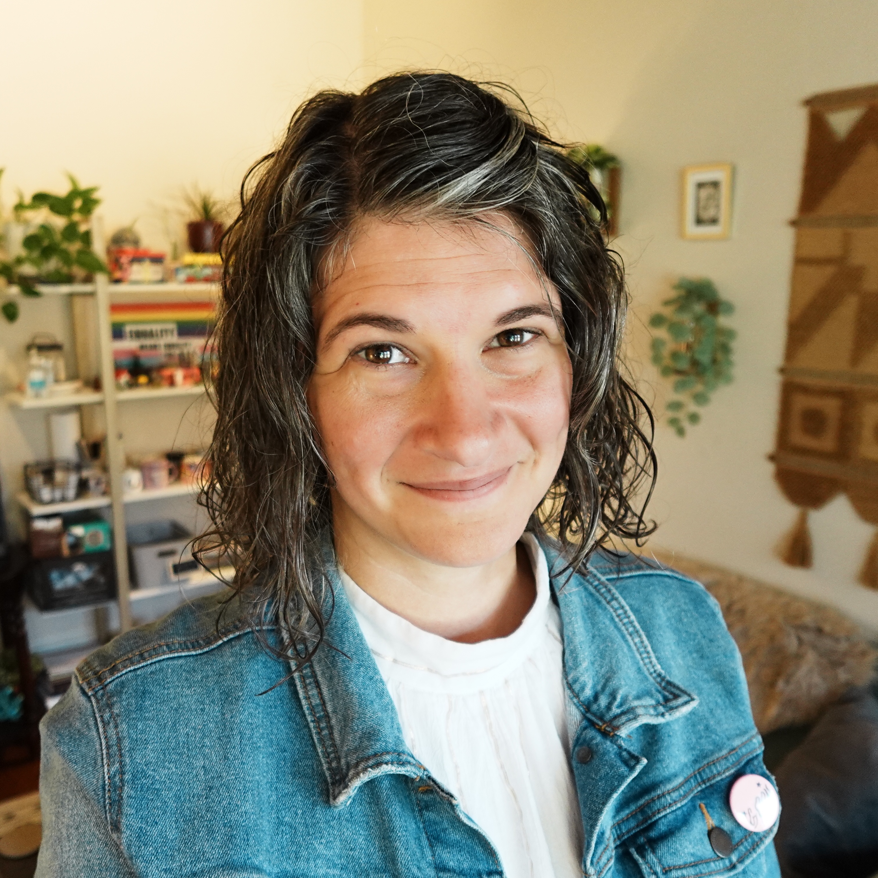 Malia Hagen, a therapist, stands smiling in her office with books and plants all around.
