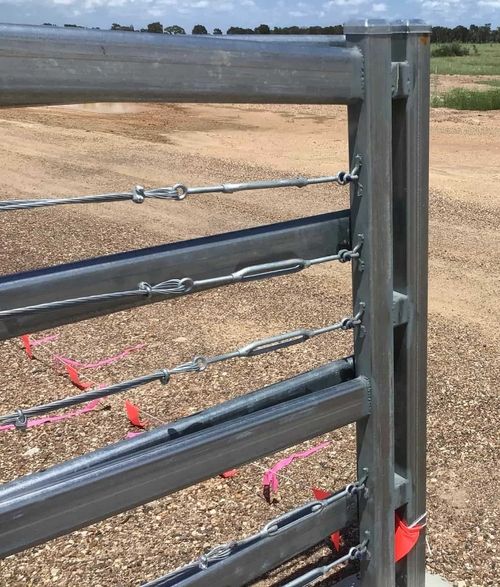 close-up image of steel gate meeting the fence. there is graded dirt in the background