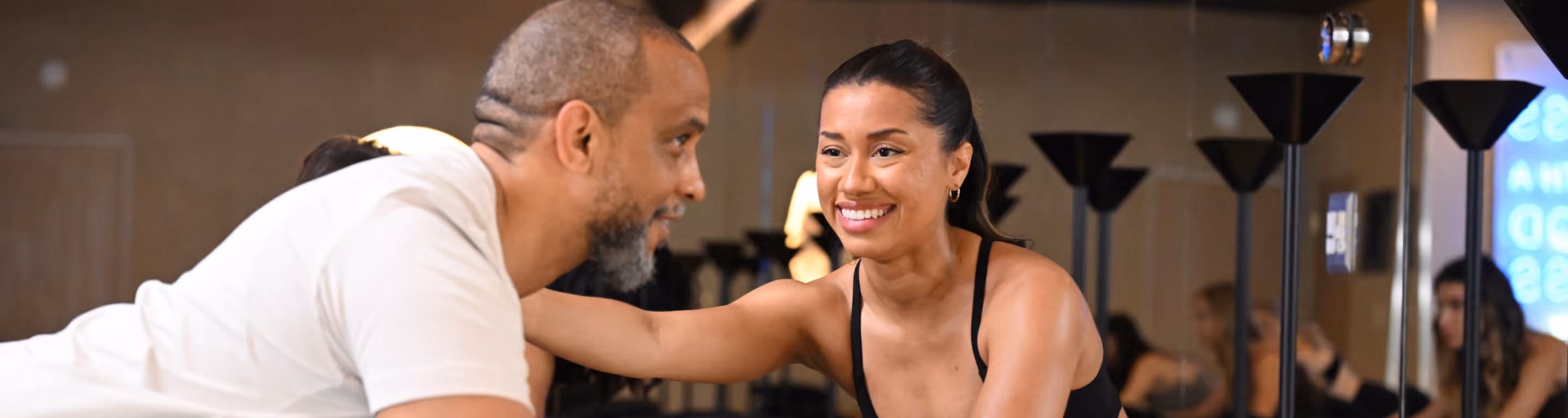 Smiling woman in sportswear encouraging man during a workout in a gym with mirror background.