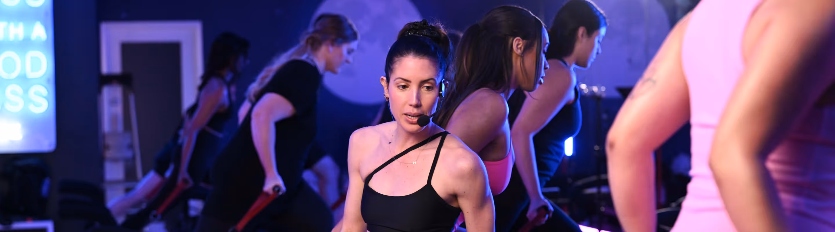 Fitness instructor with headset leading a group workout class in a dimly lit gym.