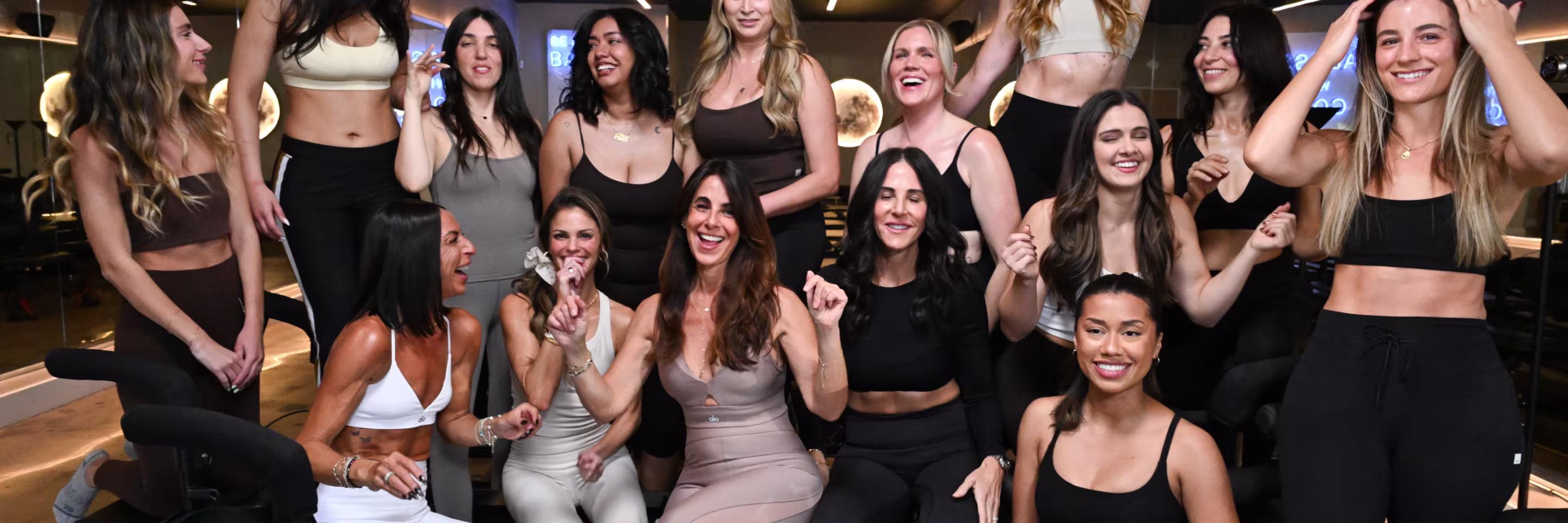 Group of smiling women in workout clothes posing and enjoying time in a gym setting.