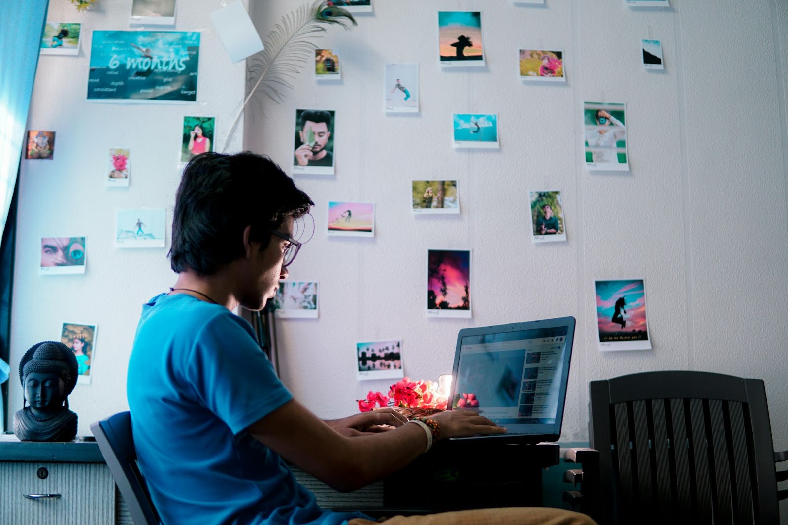 A young person watches Youtube in a dimly lit room next to a photo-covered wall.