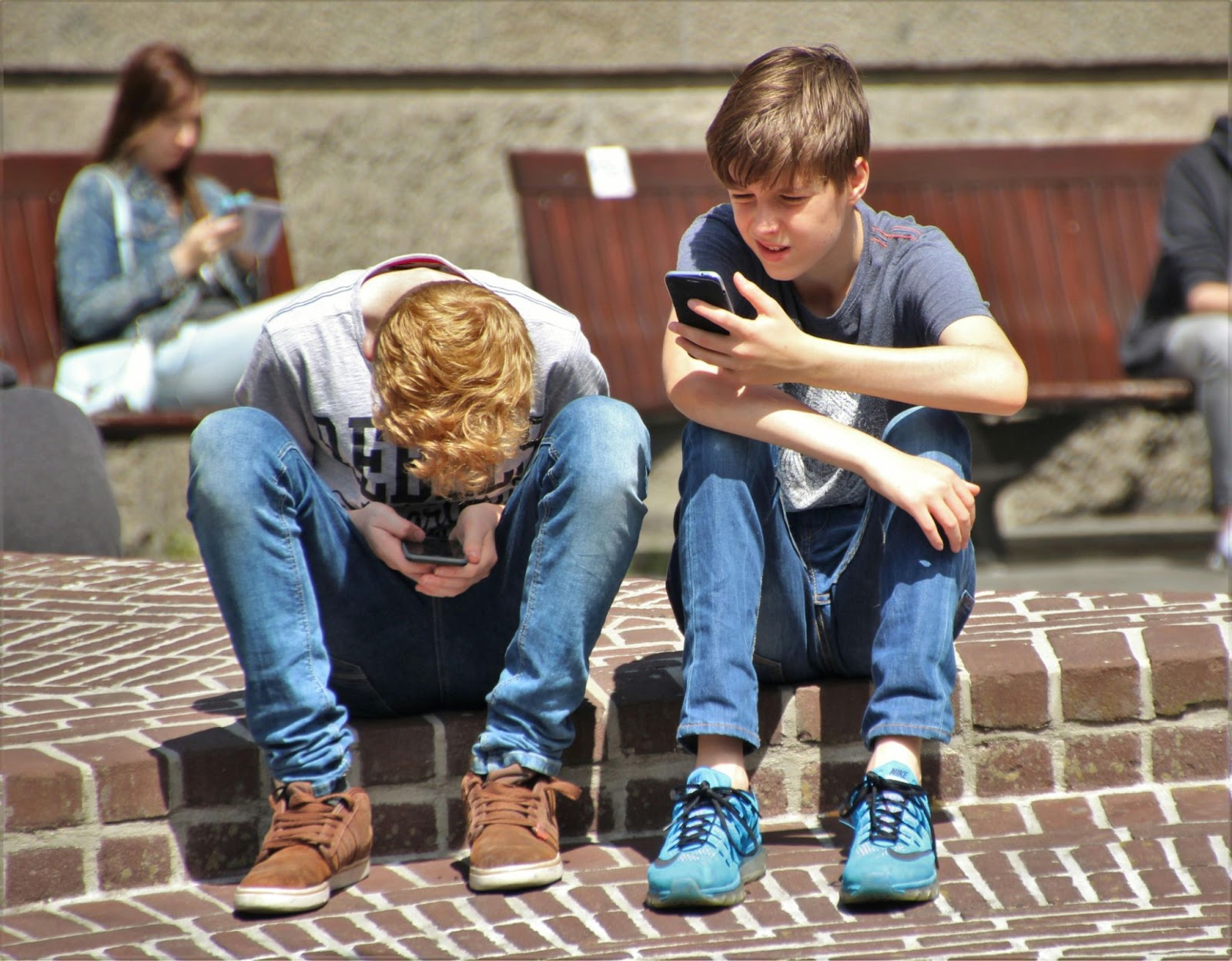 Two students look at the cell phones will sitting on a curb outside of school.